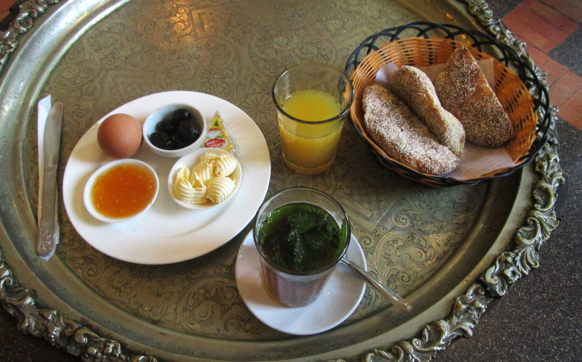 A Moroccan breakfast with bread and jam, olives, mint tea, fresh orange juice, and an egg